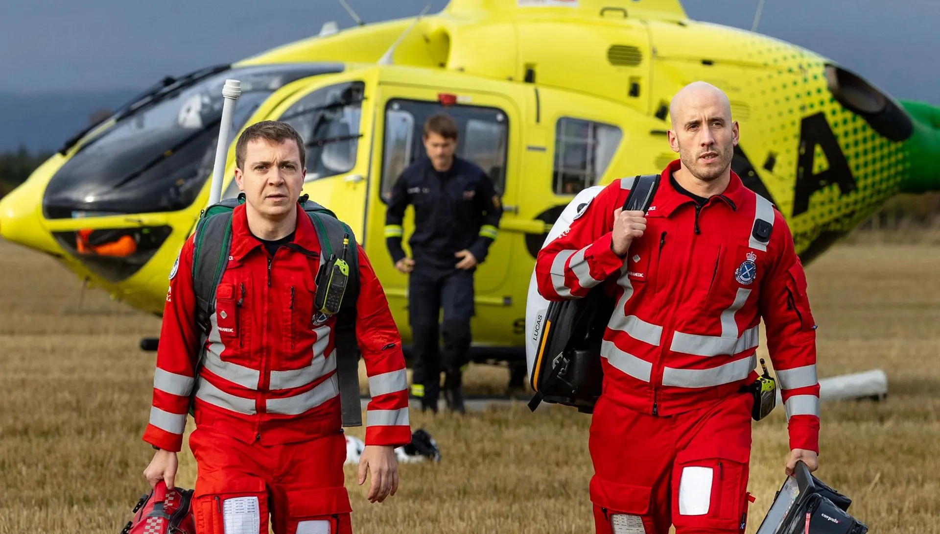 Scotland’s Charity Air Ambulance paramedics walking from their helicopter after landing in a rural field, representing the charity’s life-saving mission.