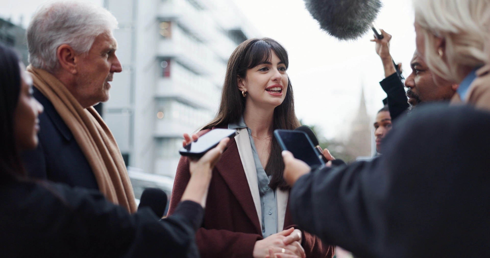 A female interviewee surrounded by journalists holding microphones and phones for a street interview.