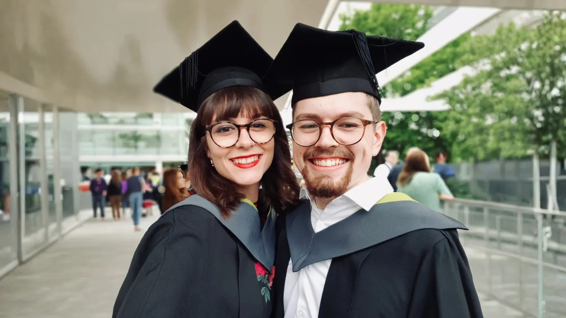 Gaby Frylinck and her husband smiling at her graduation ceremony, both wearing academic gowns and mortarboards.