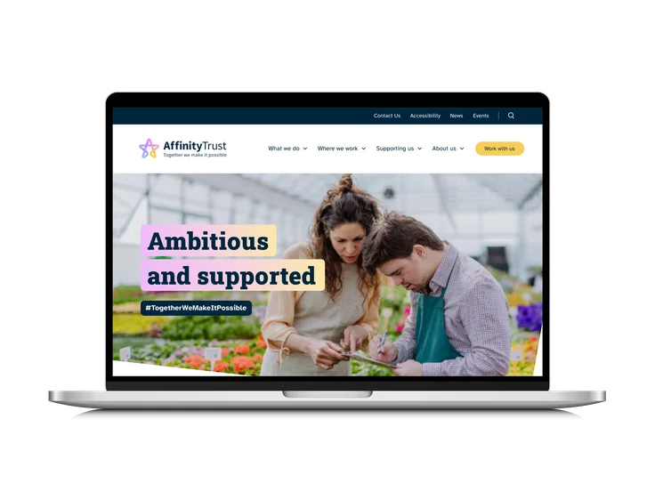 A laptop showing the Affinity Trust homepage, with "Ambitious and supported" headline over a photo of two people working in a greenhouse.