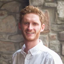 Gwilym, Business Development Director at Giant Digital, stands in front of a brick wall, smiling, wearing a white shirt.