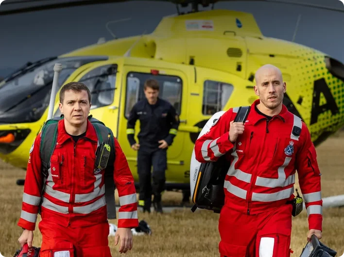 Two Scotland’s Charity Air Ambulance crew members in red uniforms walking from a yellow helicopter, used as a small case study image.