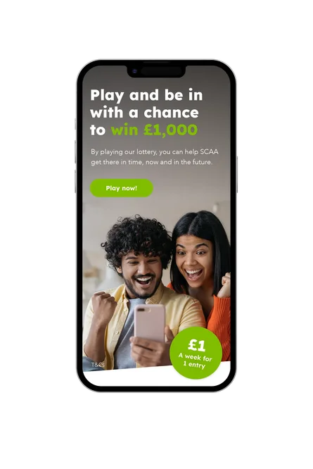 Mobile phone displaying SCAA lottery promotion with headline about winning £1,000, a green ‘Play now’ button, and a photo of two people celebrating while looking at a smartphone.