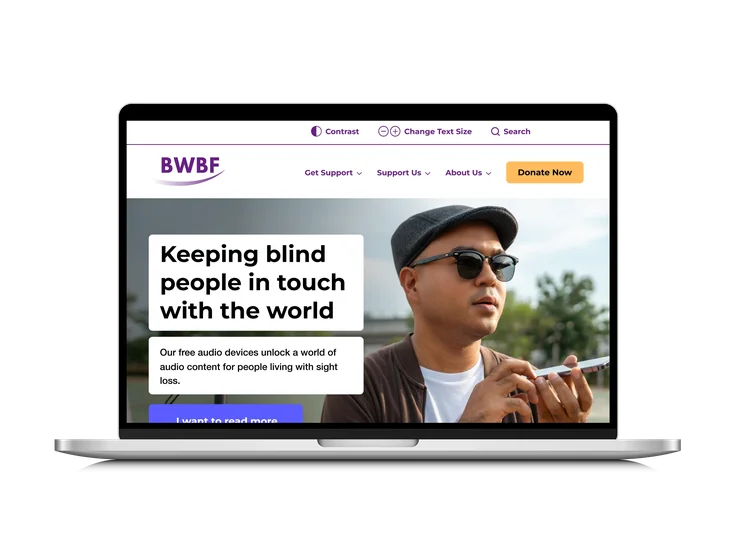 A laptop showing the British Wireless for the Blind Fund homepage, with "Keeping blind people in touch with the world" headline, accessibility controls, and a man using an audio device.