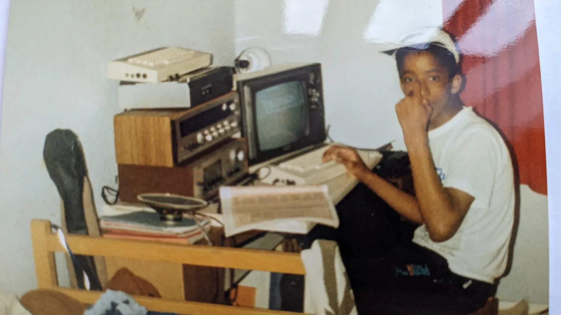 A young Wayne Fagan sitting at a desk with an early home computer setup, including a monitor, keyboard and hi-fi equipment.