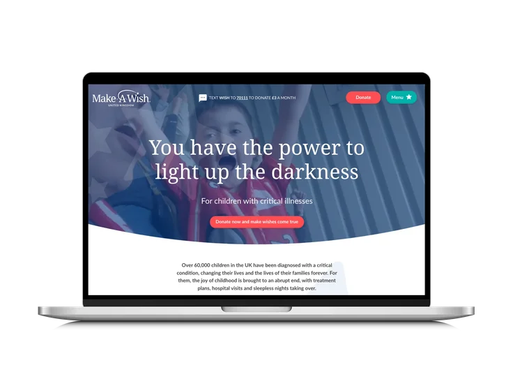 A laptop showing the Make-A-Wish UK homepage, with "You have the power to light up the darkness" headline over a photo of a cheering child.