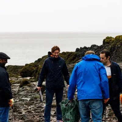 Giant Digital team members taking part in a beach clean, standing on a rocky shoreline wearing gloves and outdoor clothing while collecting litter.