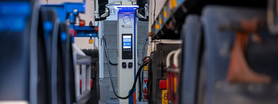 An EV charging point between two parked electric trucks in a depot.