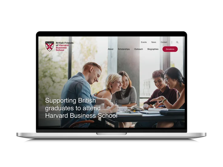 A laptop showing the British Friends of HBS homepage, with "Supporting British graduates to attend Harvard Business School" headline over a photo of students studying.