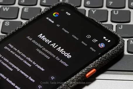 A smartphone screen displaying Google's AI Mode interface with the headline "Meet AI Mode" and example prompts, placed on top of a laptop keyboard.