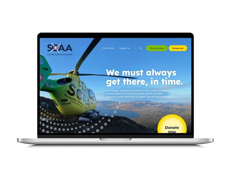 A laptop showing the Scotland's Charity Air Ambulance homepage, with "We must always get there, in time" headline over a helicopter on a hillside, and a Donate now button.