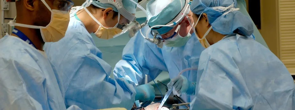A surgical team in scrubs, masks and headlamps performing an operation in an operating theatre.