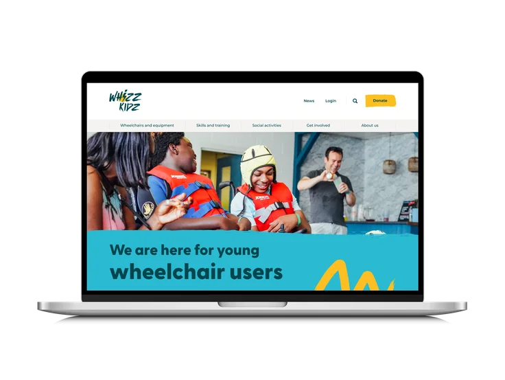 A laptop showing the Whizz Kidz homepage, with "We are here for young wheelchair users" headline, main navigation, and young wheelchair users at a water activity.