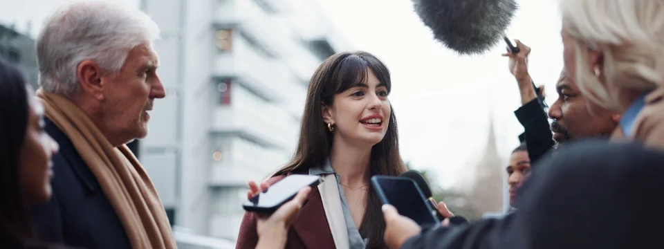 A female interviewee surrounded by journalists holding microphones and phones for a street interview.