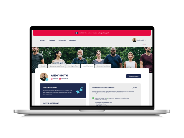 A laptop showing the Help for Heroes My Recovery portal profile page for Andy Smith, with accessibility questionnaire details and a group photo of participants.