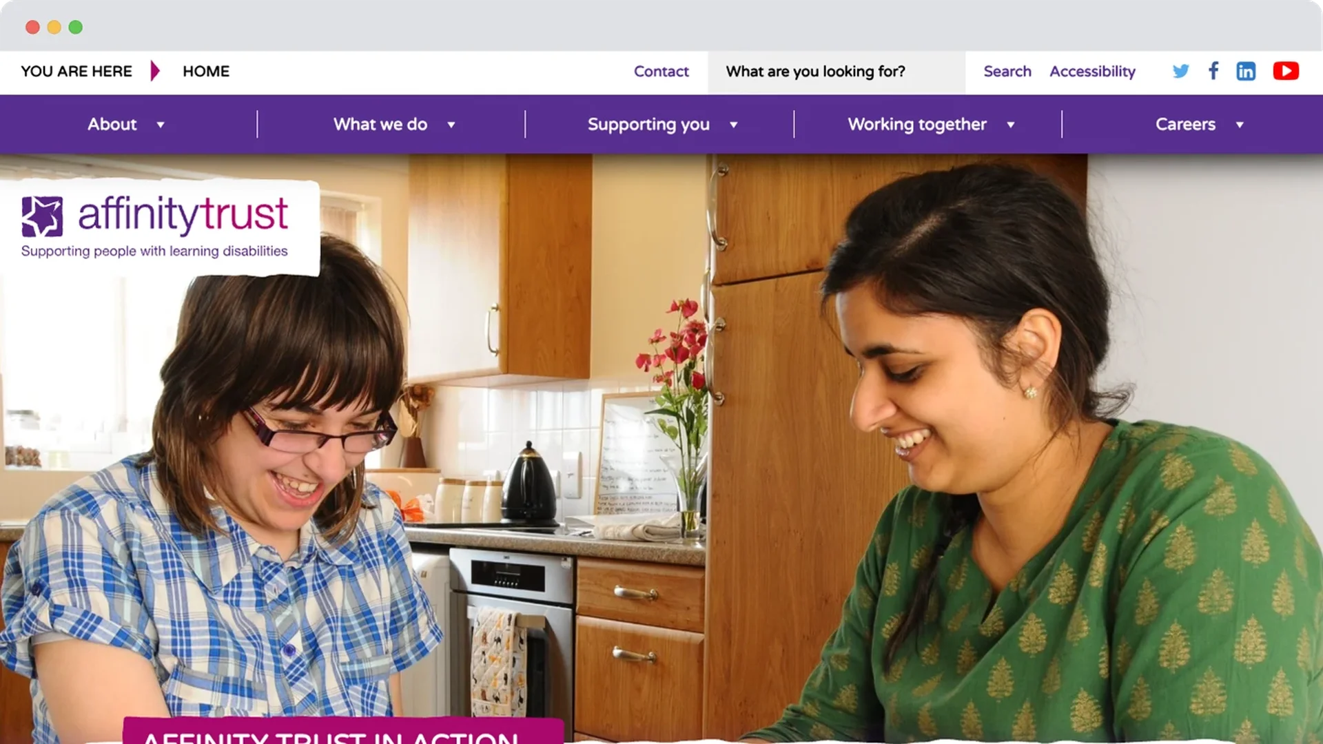 An image showing Affinity Trust's old website design. A young woman with learning disabilities smiles at the kitchen table alongside a support worker. They’re enjoying a shared activity in a warm, homely environment.