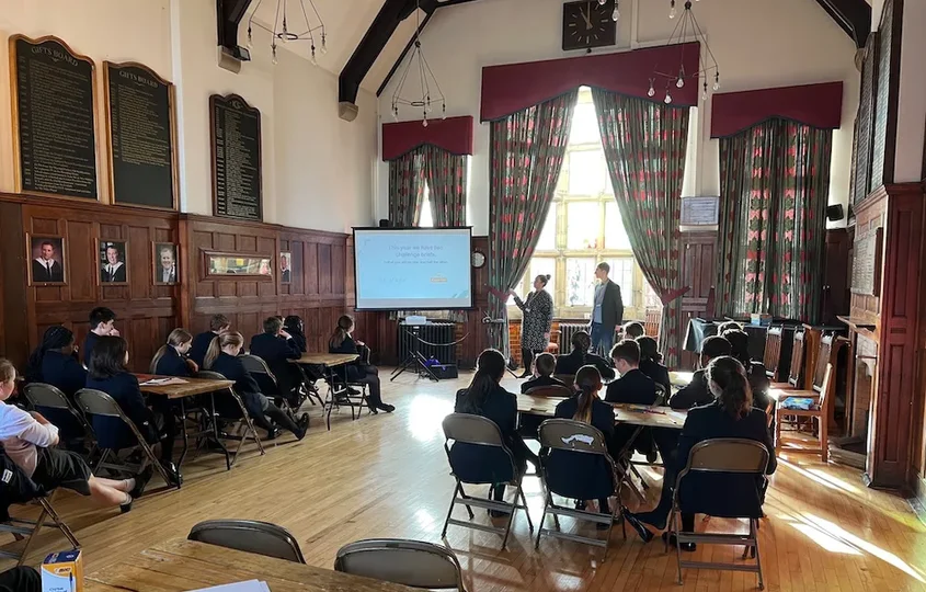 Lally, our Operations Director, delivering a session to students at Kirkham Grammar School as part of BIMA Digital Day, with pupils seated at tables and presenters speaking at the front of the hall.