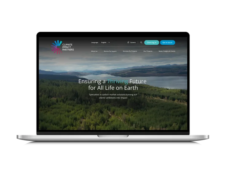 A laptop showing the Climate Impact Partners homepage, with "Ensuring a Thriving Future for All Life on Earth" headline over an aerial forest and loch image.