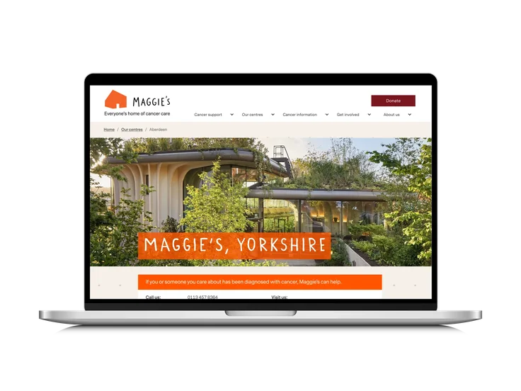 A laptop showing the Maggie's Yorkshire centre page, with an exterior photo of the building and contact details below.